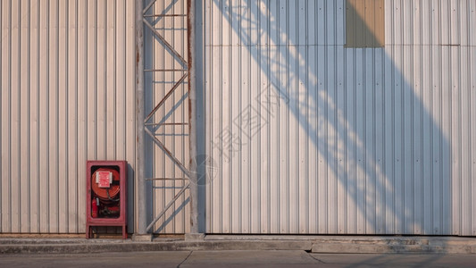 古老的红色应急柜子和在水泥地板上有阳光和影子的铁板墙壁表面水泥地板上锈制金属高地路标牌结构工厂建筑的金属板墙壁表面有阳光和阴影工背景图片