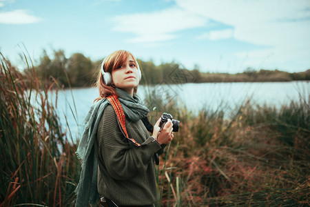 年轻女子在森林里拍照用旧的模拟相机和耳拍摄户外肖像红发女郎雀斑高清图片素材