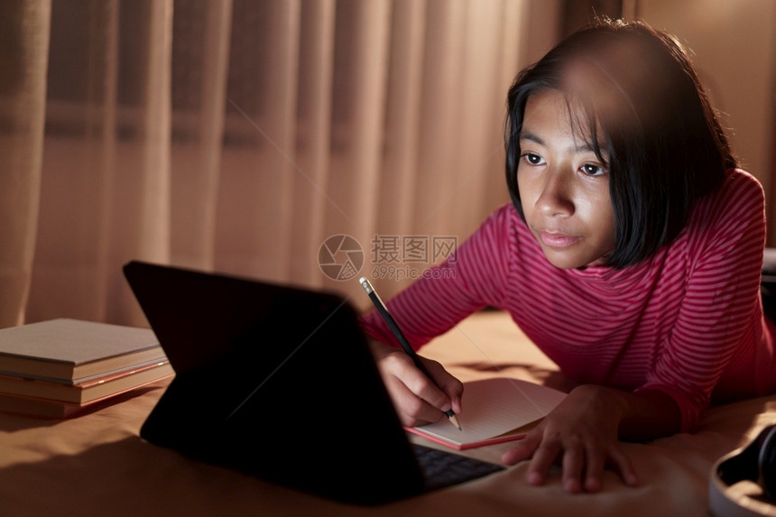 老师亚裔女孩躺在床上做家庭作业在晚上睡觉和做家庭作业时透过互联网在平板电脑上学习在家网的概念亚洲人卧室图片