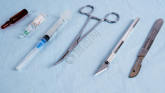 已消毒卫生刀片夹子针筒和蓝色拉皮织物上的注射器解剖刀图片