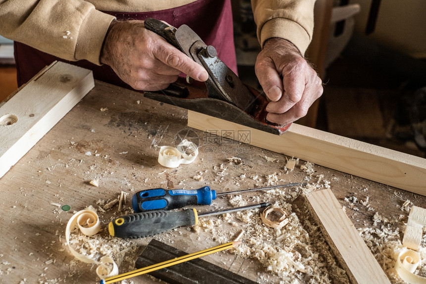 细木工雕刻匠男子用手平板工具和木刮碎卷的材废料工人图片