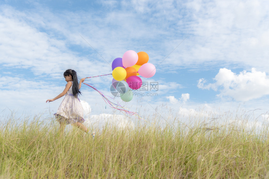 活动红色的一种快乐女孩在一片充满云彩蓝天的绿草地上拿着多彩空气球图片