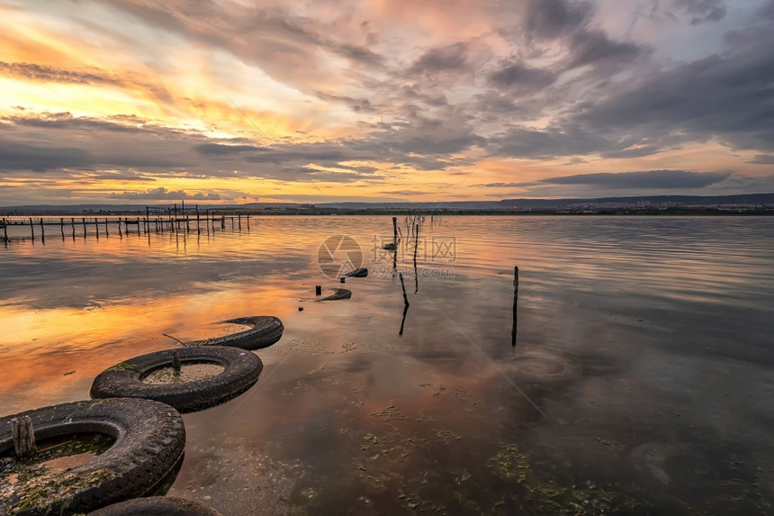 旅行感人的湖边美丽日落水里和旧轮胎有渔网反射图片