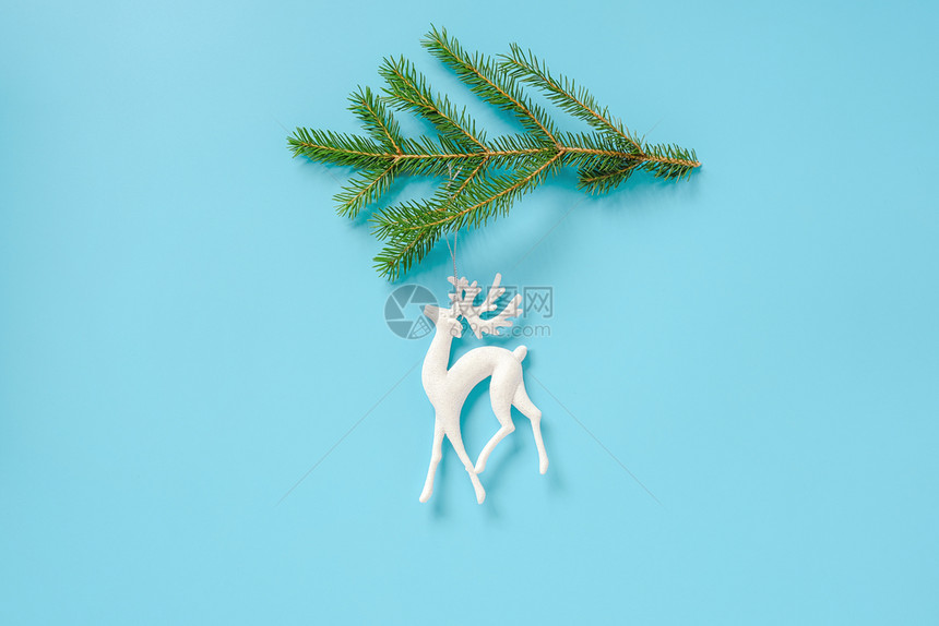 分支为了蓝色背景冷杉树枝上的白色圣诞装饰鹿玩具与复制空间概念圣诞快乐或新年最小风格顶视图平躺模板设计卡片邀请白色圣诞装饰鹿玩具在图片