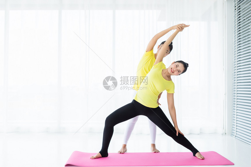 人们两名亚洲年轻妇女在健身房练习瑜伽穿黄色礼服或与训练员和实习者一起表演冥想健康生活方式和健康概念团体老师图片