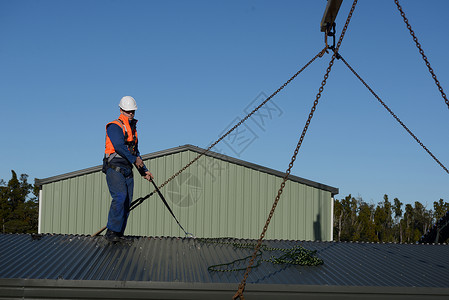 多于商人技能一名身着安全套带的建筑工帮助将吊环放置在起重机上以便提升携式建筑物背景图片