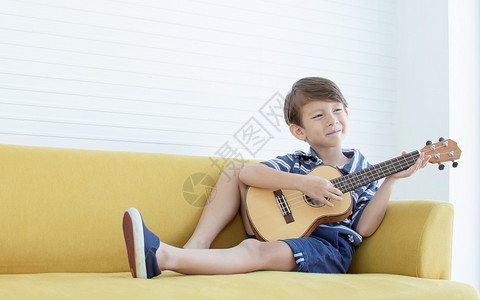 音乐活的唱歌在家中客厅的黄色沙发上弹吉他时Caucasians男孩的肖像很快乐爱好高清图片素材