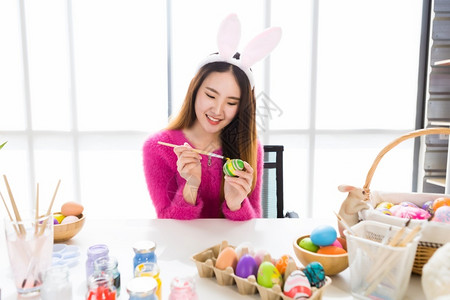 女孩兔子复活节的概念带着兔子耳朵的亚洲快乐年轻女披着兔子耳朵的青春少女为复活节画了鸡蛋在白衣室背景下可爱的年轻季节背景
