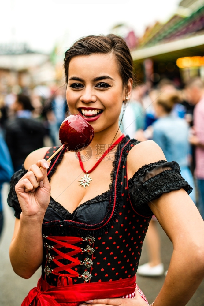 游乐场肖像有魅力的年轻女在Oktoberfest盛宴上拿着红焦糖苹果和背景中的人在一起Oktoberfest有吸引力的年轻女吸引图片