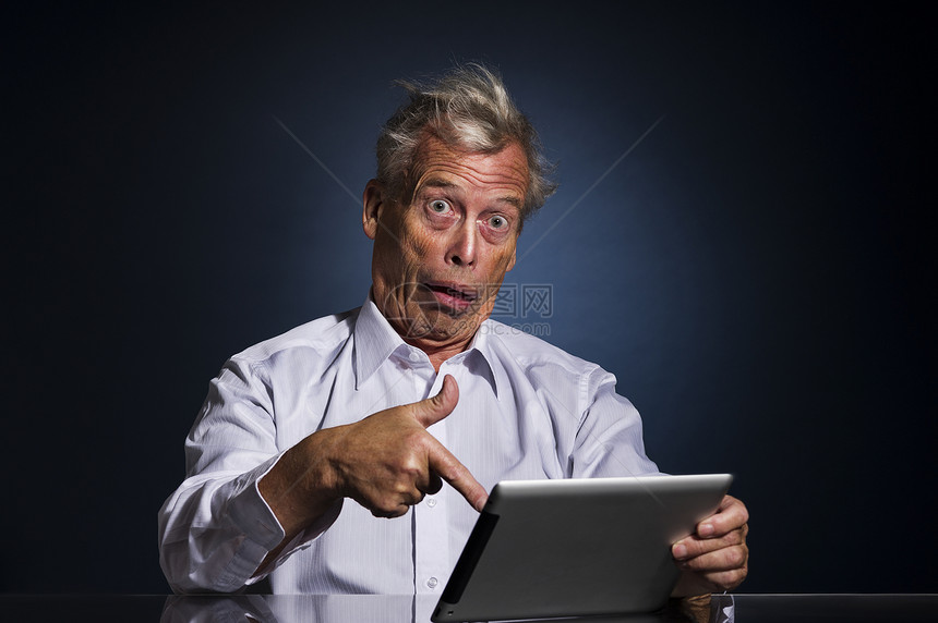 惊喜商业傻的震惊老人用他手指着平板电脑看令人惊骇的难以置信和混乱幽默的上身工作室肖像画图片