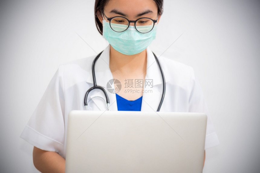 灰色的亚洲年轻女医生佩戴眼镜和面具保护科罗纳的安全看笔记本电脑有听诊器的医生正在用一台电脑来阻止Covid19的流行医生正在用一图片