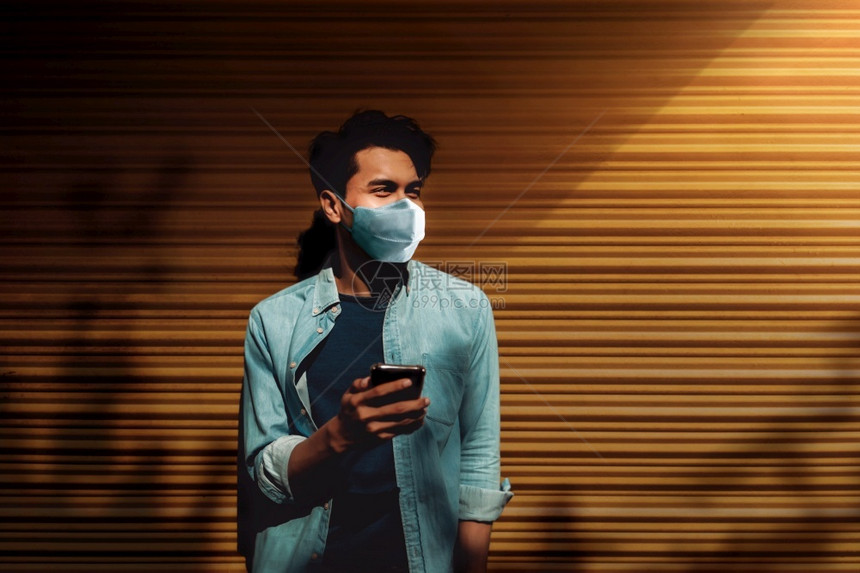 沟通冠状在新的正常生活方式概念中亚洲年轻人穿着外皮面具和使用智能电话站在夏期保健中反对黄墙的新型普通生活方式概念时图片