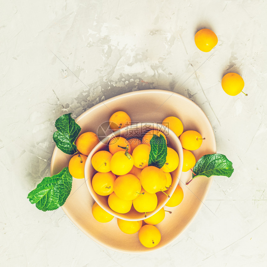 躺着李子以粉红色碗中新鲜黄樱桃羽在灰色混凝土底灰色水泥上创造的夏日模式水果最小概念食物图片