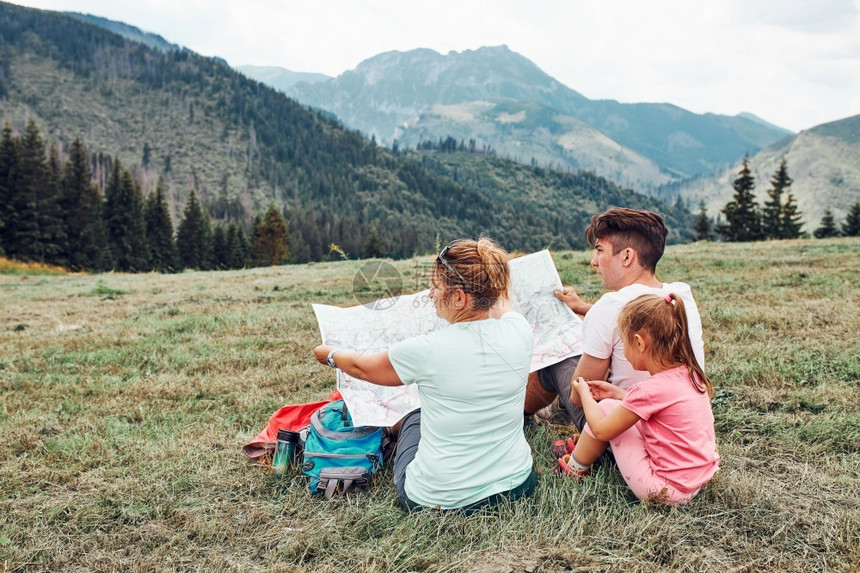 喜悦白种人一家在山区度假旅行期间坐在草地上查看山区试验人们在山上度假期间积极地在户外度过时间女孩图片