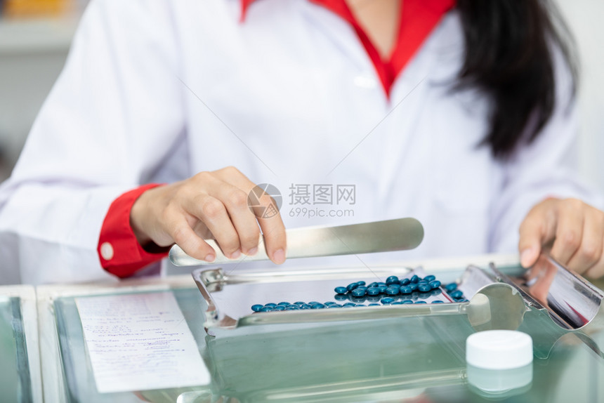 制服泰国药店柜台的亚洲女药剂师物计数和包装盒架子图片
