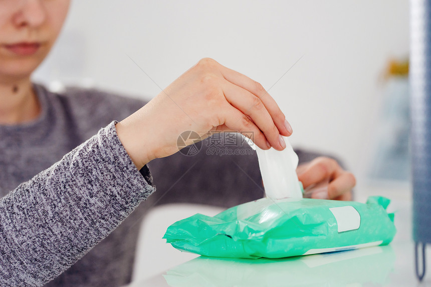 女士在家中或办公室的防菌消毒酒精卫生产品中从白架子上的箱式集装包里取湿纸巾组织手举着不明女在家中或办公室抗菌消毒酒精卫生产品或者图片