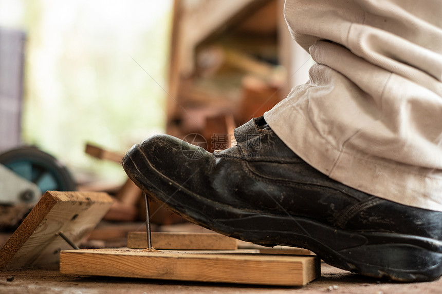 覆盖工匠在建筑区用安全鞋踩板木上钉子的工人警告锋利图片