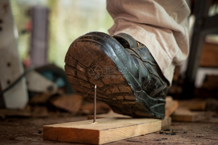 地点木制的工作匠在建筑区用安全鞋踩板木上钉子的工人图片