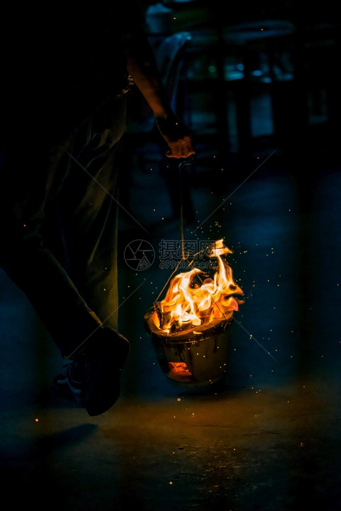 男人手握着燃烧的炭烤炉在黑暗背景下用火焰和点烧做饭焦质地图片