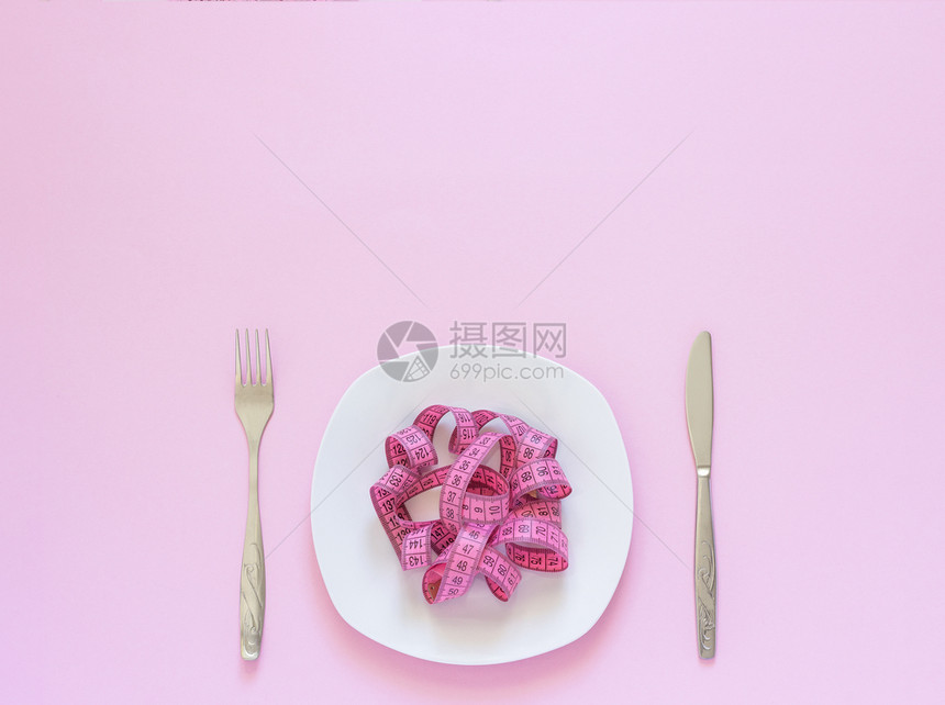 重量粉色测磁带放在盘子上以意大利面刀和叉为形式在粉红背景上用面刀和叉作为形式的面粉刀和叉作为红色背景上用餐或厌食概念损失贪症图片