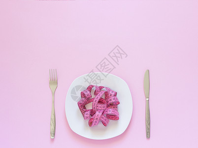重量粉色测磁带放在盘子上以意大利面刀和叉为形式在粉红背景上用面刀和叉作为形式的面粉刀和叉作为红色背景上用餐或厌食概念损失贪症生病的高清图片素材