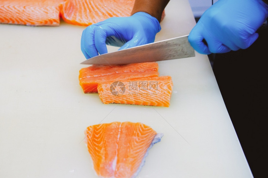 蛋白质切沙门鱼片主厨切开新鲜生鲑鱼片餐桌上的剪板有一把尖利刀手紧寿司新鲜的图片