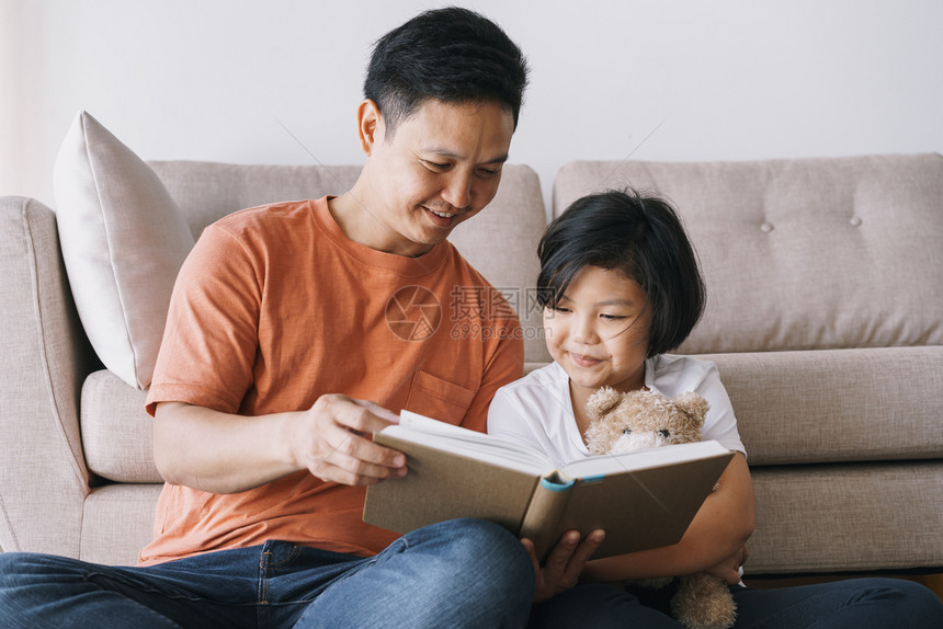 家庭亚裔父亲和女儿在家中客厅读书时坐在起居室肖像粘合图片