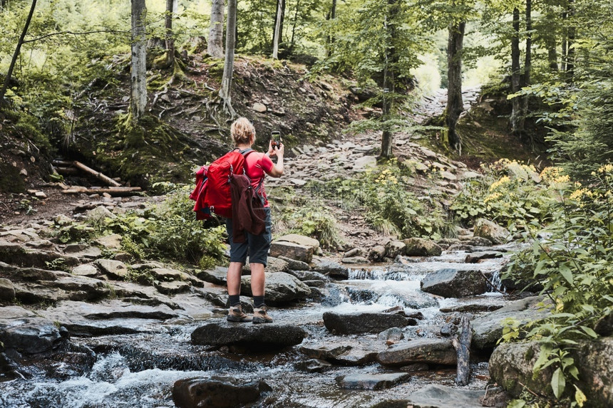 在夏季旅行中使用智能手机相在山上岩站立于拍摄度假女人的照片和背着包拍照的景观片闲暇活动服用图片