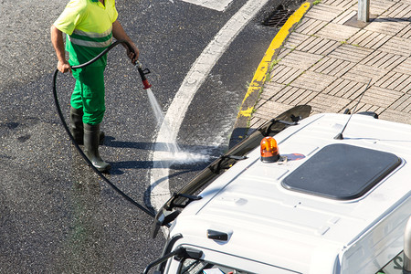 肮脏的工人用高压水清洗道路和街人行的清洁工洗涤公司图片