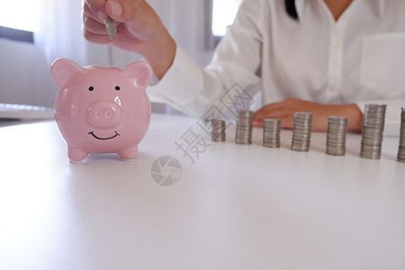 钱会计商业人员在小猪银行与办公桌堆叠的纸箱中插入硬币扑满图片