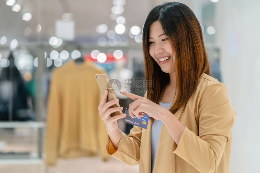 交易扫描东南亚洲妇女利用信卡和移动电话在百货商店通过服装背景技术钱财包和网上支付概念信用卡模型在线购物亚洲妇女使用信卡和移动电话图片