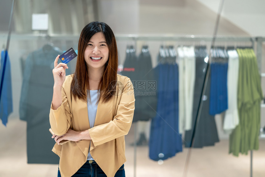 移动的女士网络利用带有智能手机的信用卡在百货商店通过服装铺背景技术资金钱包和在线支付概念购物的亚洲妇女肖像信用卡以及智能移动电话图片