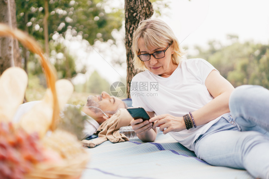 年龄男人在公园使用智能手机的老人夫妇在公园中一起使用智能手机老年夫妇在夏季白天放松退休后生活方式的概念得到放松年长夫妇在暑夏光日图片