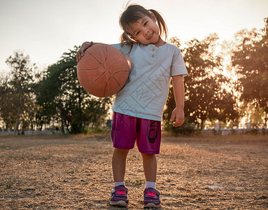 幼儿篮球学习幸福一种穿运动服篮球和看夏季公园照相机的亚洲可爱小女孩为幼儿提供健康户外运动体育为幼儿提供健康运动背景