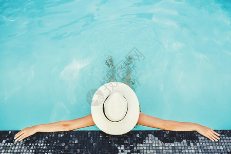 泳装女人戴着大帽子在泳池放松背景图片