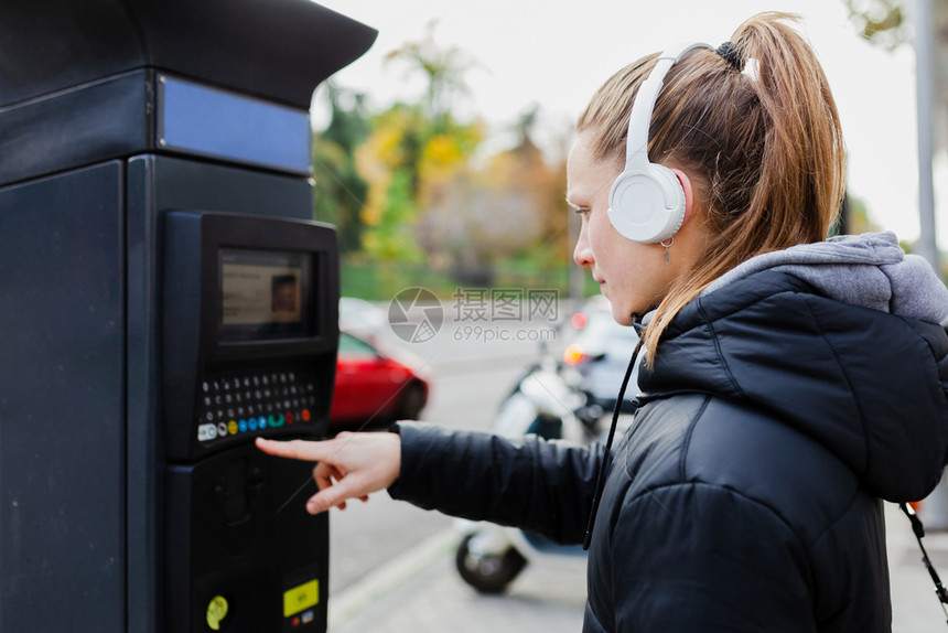 外部积极的快乐年轻金发美女在城里付停车费脸上戴着耳机的夹克脸型惊讶的图片