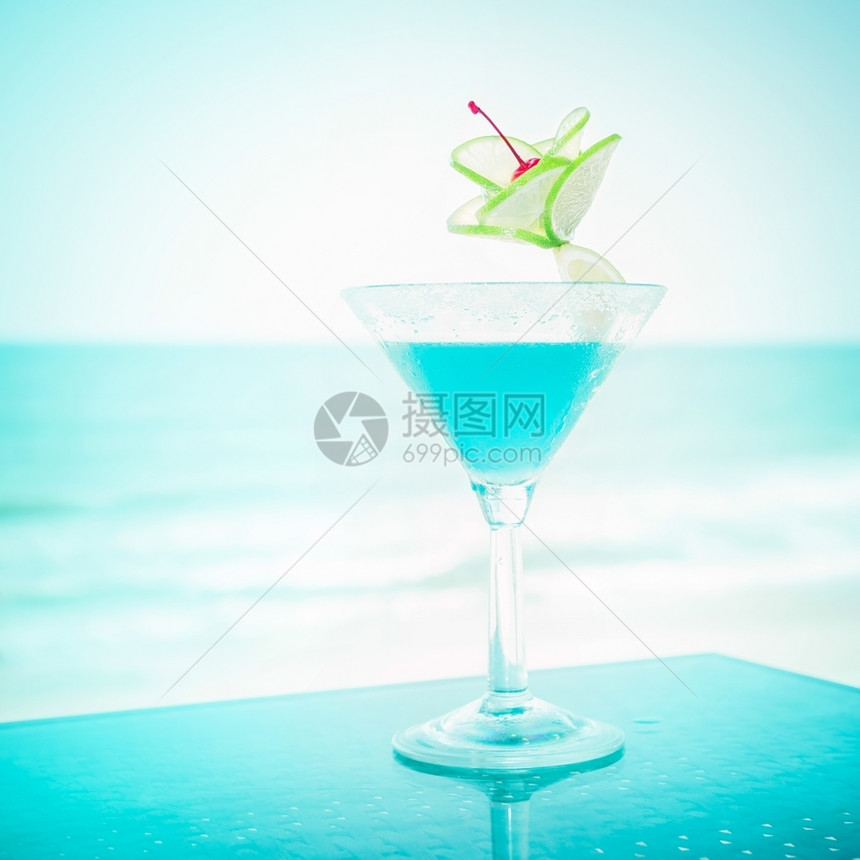 蓝色玛格丽塔鸡尾酒在热带海洋滩的滨上配有石灰水果和樱桃装饰品的蓝色玛格丽塔鸡尾酒餐厅天堂海岸图片