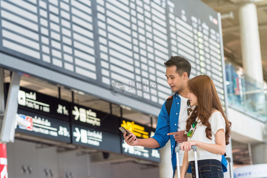 旅游飞机朋友们亚洲夫妇旅行者使用智能移动电话在机场现代飞行信息屏幕上登机旅行和带有技术概念的交通方面使用智能移动电话进行亚洲夫妇图片