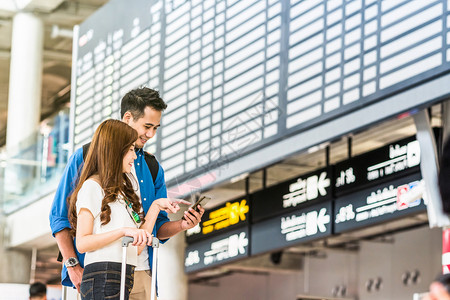 运输亚洲夫妇旅行者使用智能移动电话在现代机场飞行信息屏幕上登机旅行和具有技术概念的交通方面使用智能手机进行亚洲夫妇旅者航班飞机游客高清图片素材