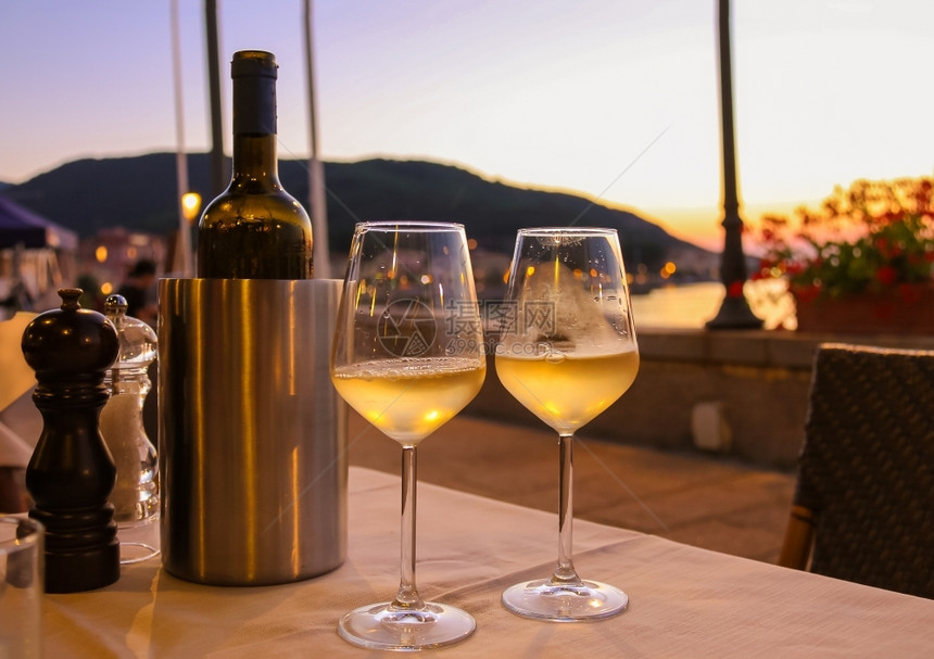 庆祝海日落时在餐桌边的白酒瓶子和两个杯目的图片