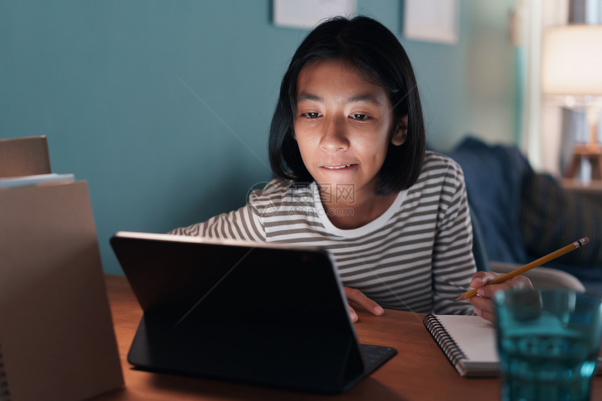 笔记本电脑在家上学的亚裔女孩晚上在书桌用平板电脑在线学习课图片