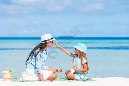 户外淑女保护不受紫外线辐射影响的概念年轻母亲对女儿在海滩上鼻子施阳光奶油年轻母亲对女儿施阳光奶油在海滩上流鼻血身体护理背景图片
