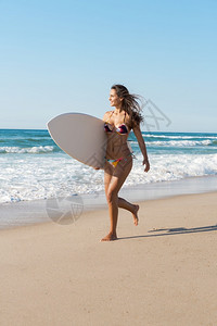 海滩上冲浪女孩拿着她的冲浪板奔跑图片