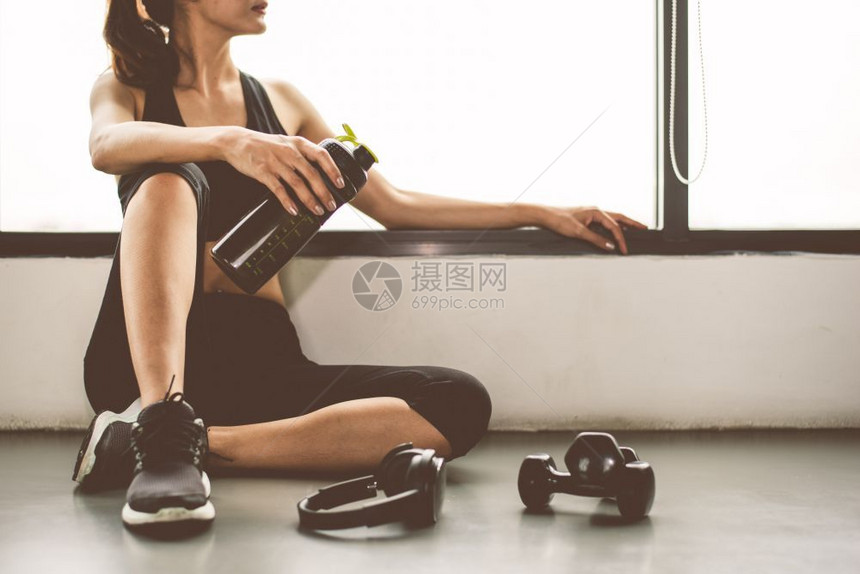打破有哑铃和机具的女在健身锻炼运动中生活方式在体育训练后放松休息以蛋白质奶昔瓶子背景进行体育培训健康生活方式的建设和运动员肌肉摇图片