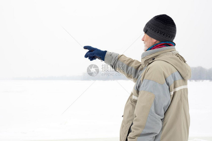一个戴羊毛帽防水夹克和羊毛帽的男人在雪下寒冷而悲伤的冬季清晨用手指靠近第尼珀尔河指着一些东西男防水的伤心图片