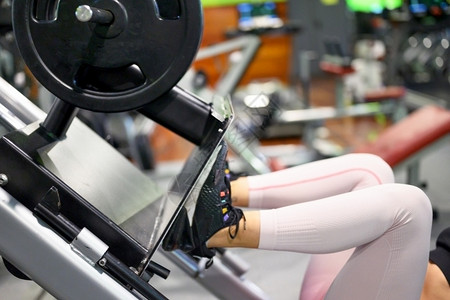 身体的强健康年轻女运动员在健身房锻炼器械上展示腿部肌肉的侧视图图片