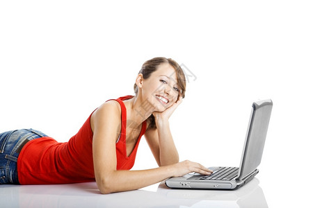 坐在地板上工作着笔记本电脑的美丽和快乐年轻女子青家请享用互联网高清图片素材