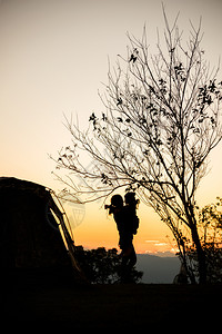 太阳外部日落时母亲与女儿拥抱在帐篷和树旁的月光下在树林山中露营冒险图片