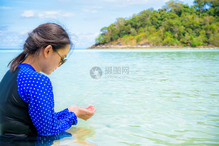 身穿蓝泳装和太阳镜的亚洲妇女在夏天前往泰国SatunTarutao公园KohLipe岛时在KoRaWi观看他们在海上手中的清水看图片