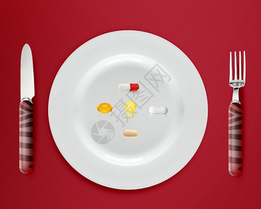 药物概念的配有红色背景药片和胶囊的餐具盘药品图片